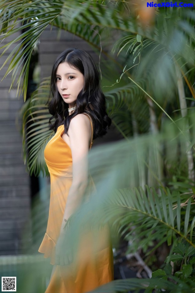 A woman in a yellow dress standing in front of a palm tree.