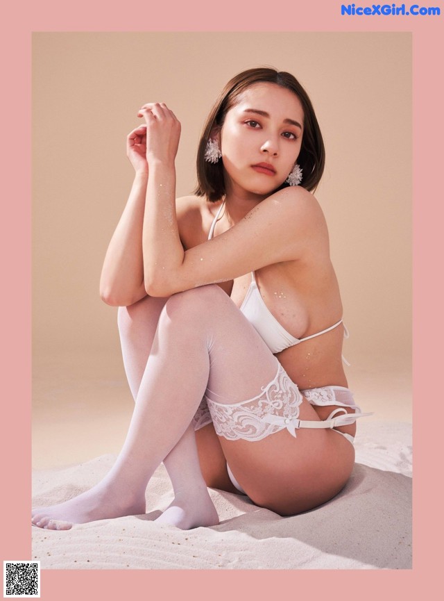 A woman in a white lingerie sitting on the sand.