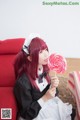 A woman sitting on a red couch holding a lollipop.