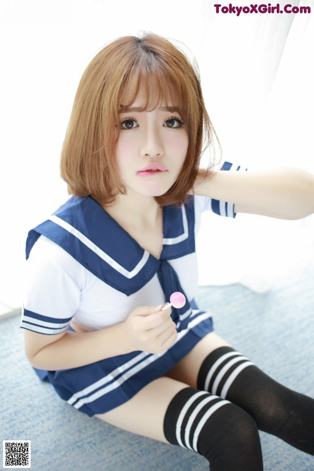A woman in a sailor outfit holding a lollipop.