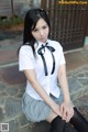 A woman in a school uniform sitting on the ground.