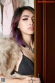 A woman with purple hair wearing a fur coat.