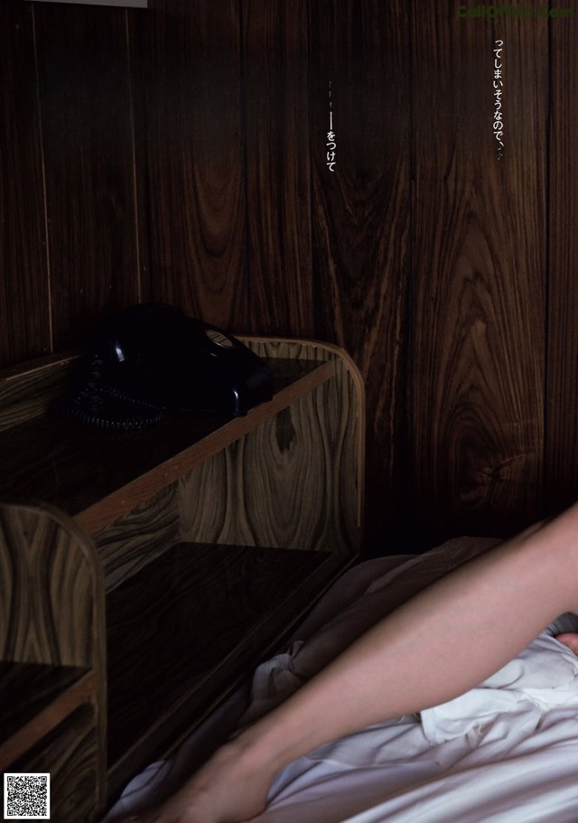 A woman laying on a bed next to a telephone.