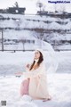 A woman sitting in the snow holding an umbrella.